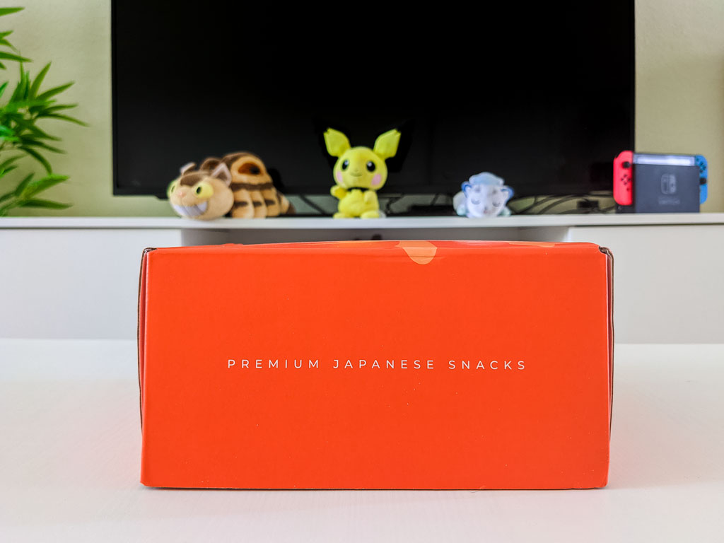 Closed orange 2021 Bokksu review box on white table, with text "Premium Japanese Snacks" written on front.