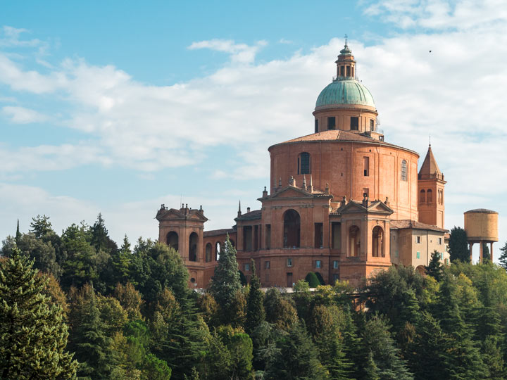 View of Sanctuary of the Madonna di San Luca with trees and blue sky, a popular Bologna sightseeing spot.