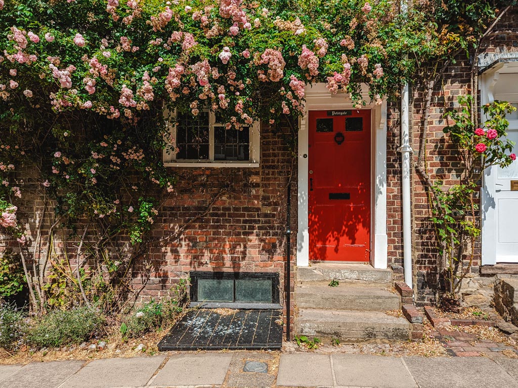 Brick UK house with red door and roses growing on facade.
