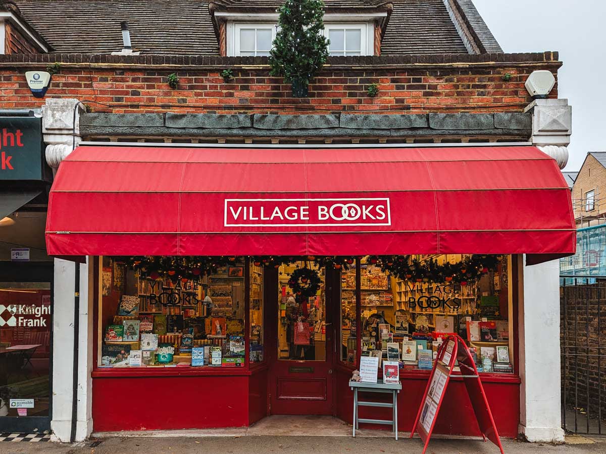 Exterior of Dulwich Village Books store with red awning and books displayed in glass windows.