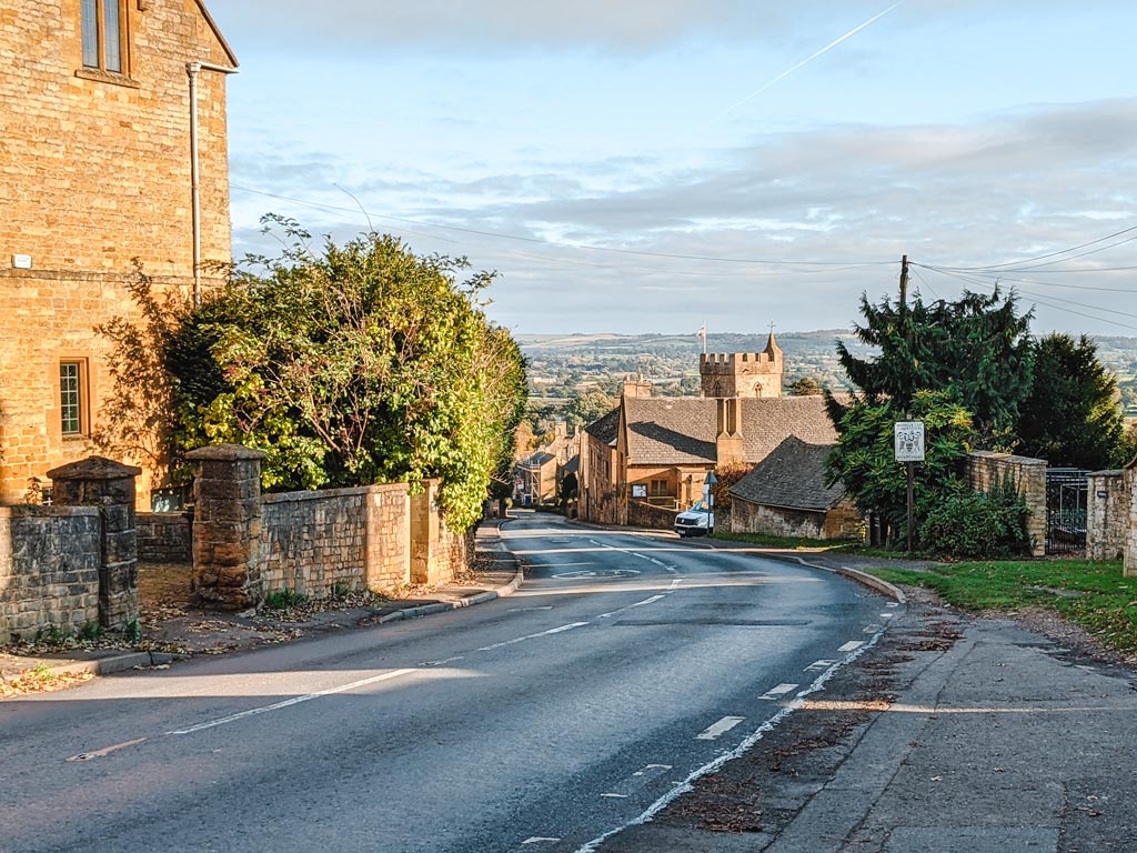 Street view of Cotswolds village on a hill overlooking countryside.