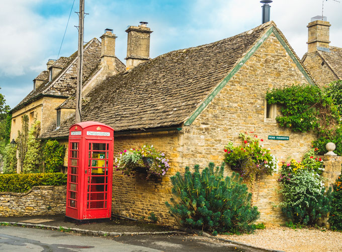 Honeyed stone cottage next to red postbox in popular village on a Cotswolds day trip itinerary.