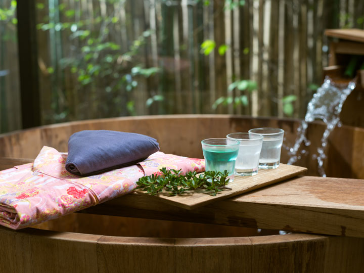 Atami wooden onsen tub with pink yukata and drinks on serving board.