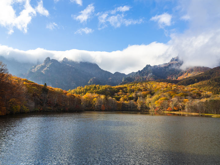 Togakushi mirror lake with autumn trees and partly cloudy sky.