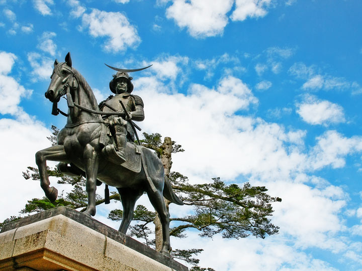 Masamune mounted on horse statue against partly cloudy sky.