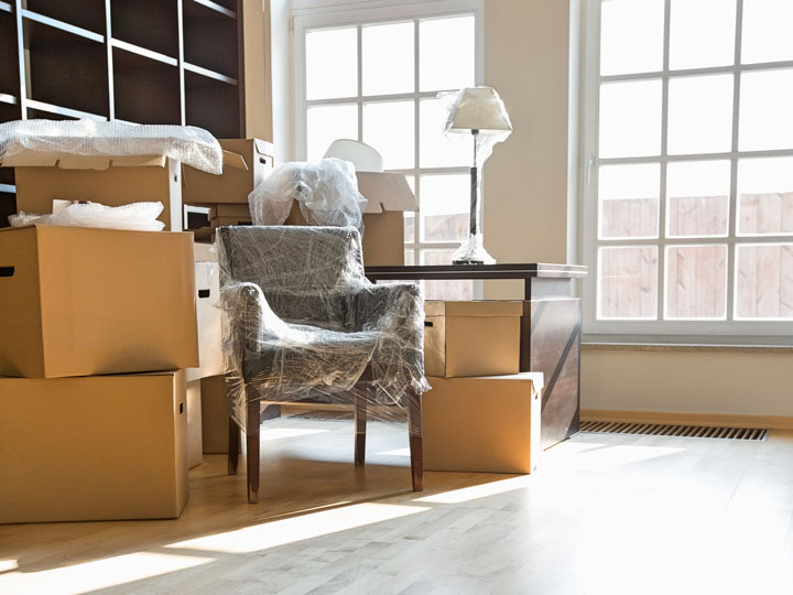 Living room with cardboard boxes stacked up and chair wrapped in plastic.