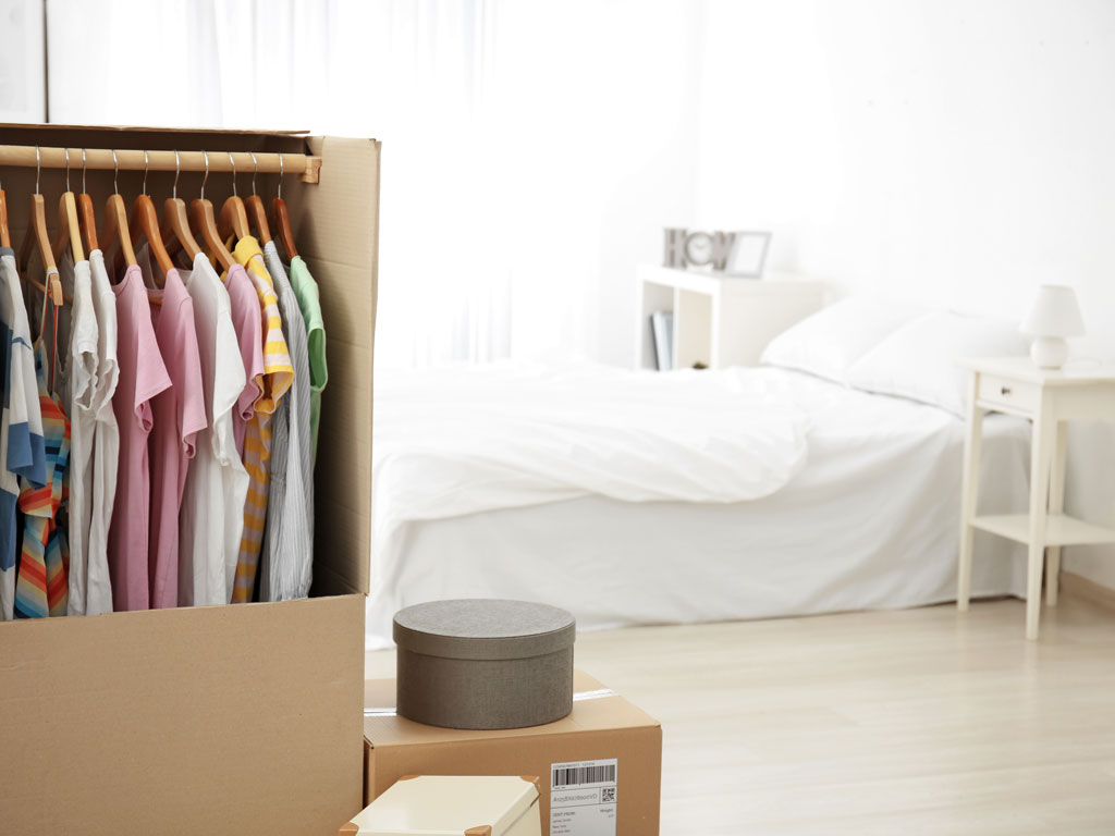 Clean white bedroom with clothes hanging in wardrobe box after decluttering before moving abroad.