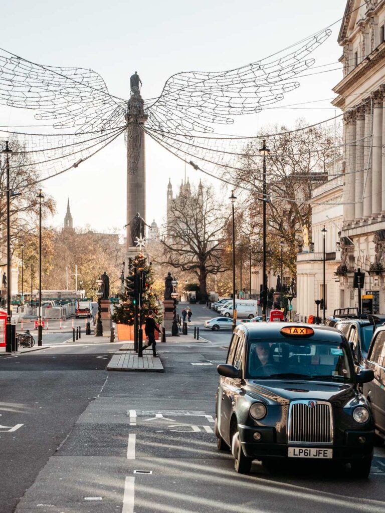 Black cab on side of London street, with angel light display and pillar in the distance.