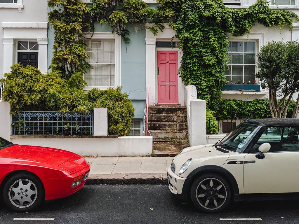 White and red cars parked outside blue row home with ivy growing around door.