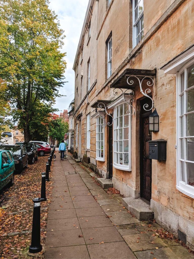 Street view of stone facades of UK row homes, with autumn leaves on sidewalk.