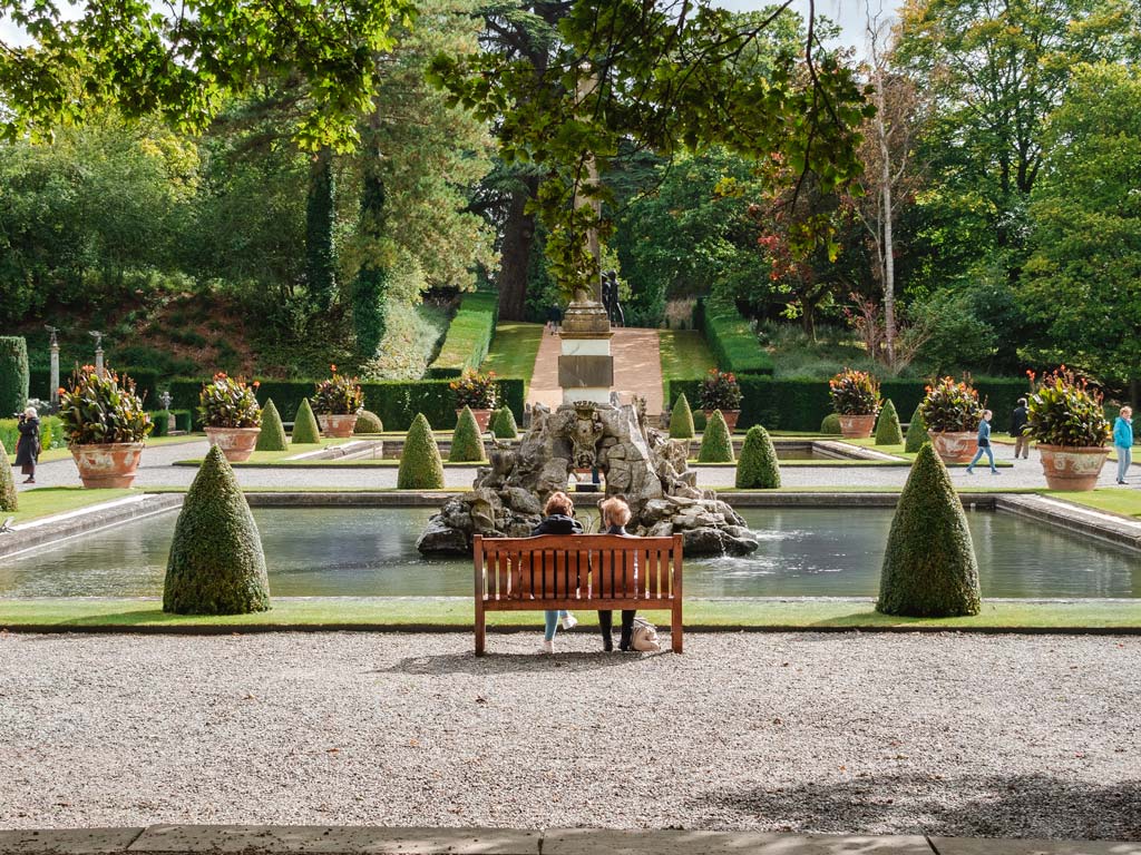 Blenheim Palace fountain and garden, with two women sitting on wooden bench.