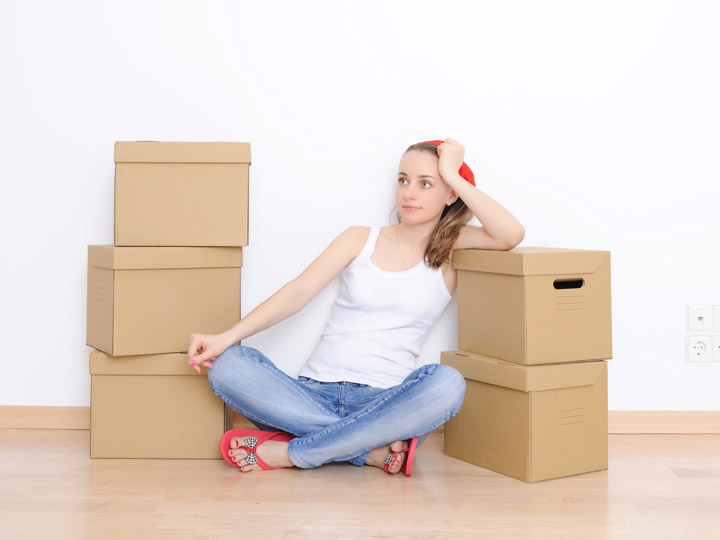 Tired girl sitting on floor with 5 moving boxes, thinking about difficulties of moving to a foreign country.