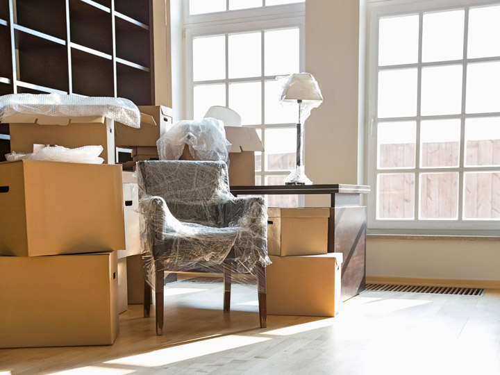 Bright room with cardboard boxes and chair wrapped in plastic for moving.