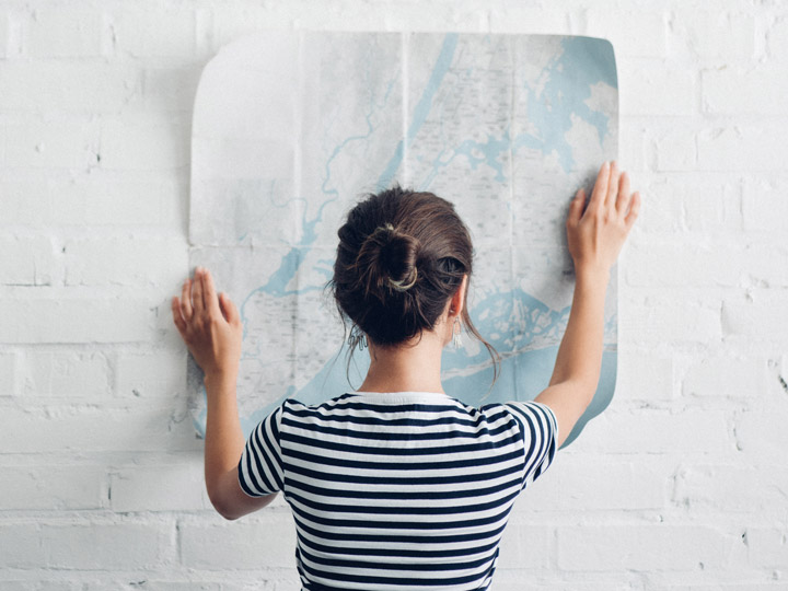 Girl in striped shirt holding map against white brick wall.