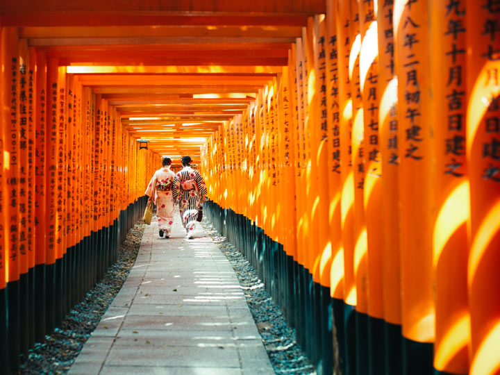 Two women in kimonos walking through orange torii gate path at Fushimi Inari.