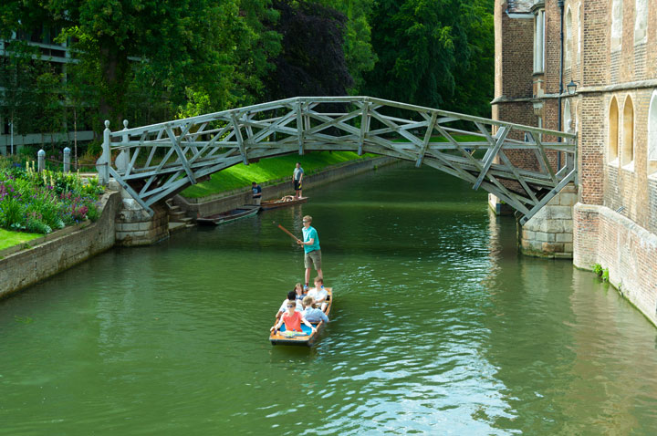 Student punting boat on Cambridge river under bridge.