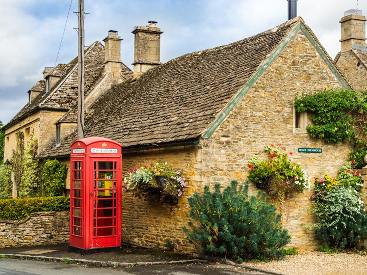 Cotswolds stone cottage with bushes and red phonebox out front.