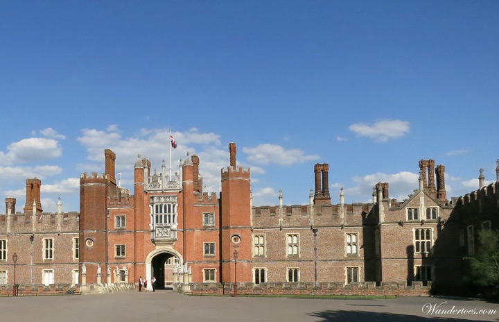 Stone facade of Hampton Court Palace on sunny day.