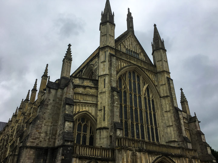 Front of Winchester Cathedral with arched windows and spires on cloudy day.