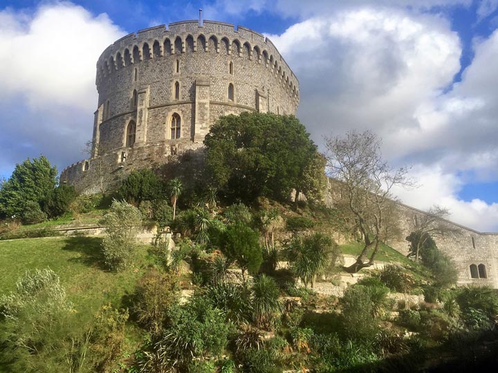 View of Windsor Castle and gardens from ground level with partly cloudy sky.