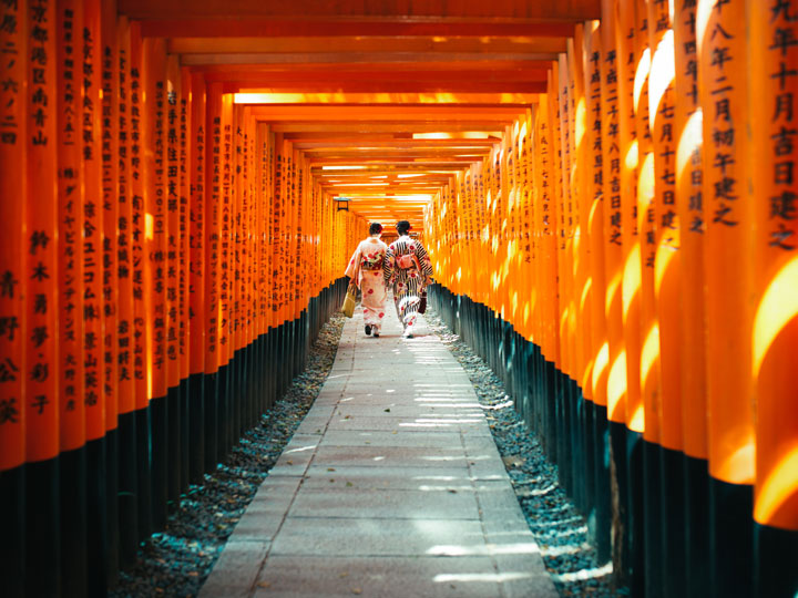 Two women in yukata walking through Fushimi Inari orange torii gates, the most famous things in Japan.