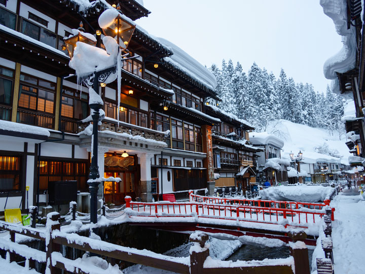 Ginzan Onsen with buildings and red bridge covered in snow.