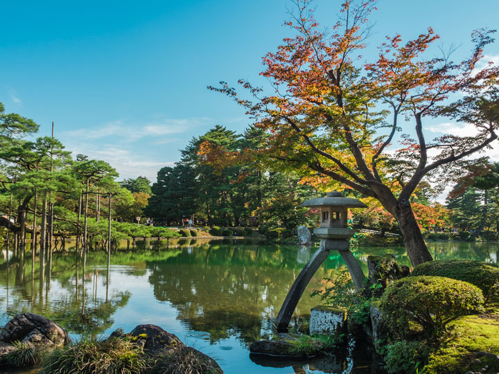 Kenrokuen Garden in Kanazawa Japan with pond, moss rocks, and autumn tree.