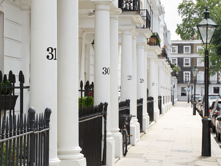 White columns with black numbers and iron fence next to London sidewalk.