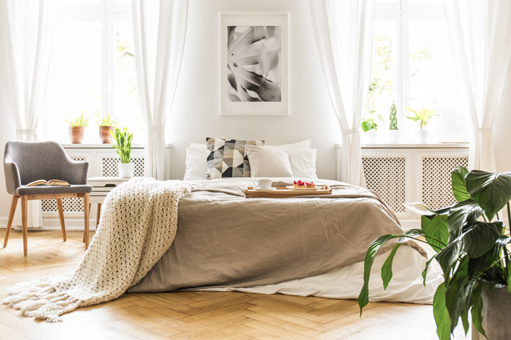 Brightly lit bedroom with white bed, grey chair, and green plant.