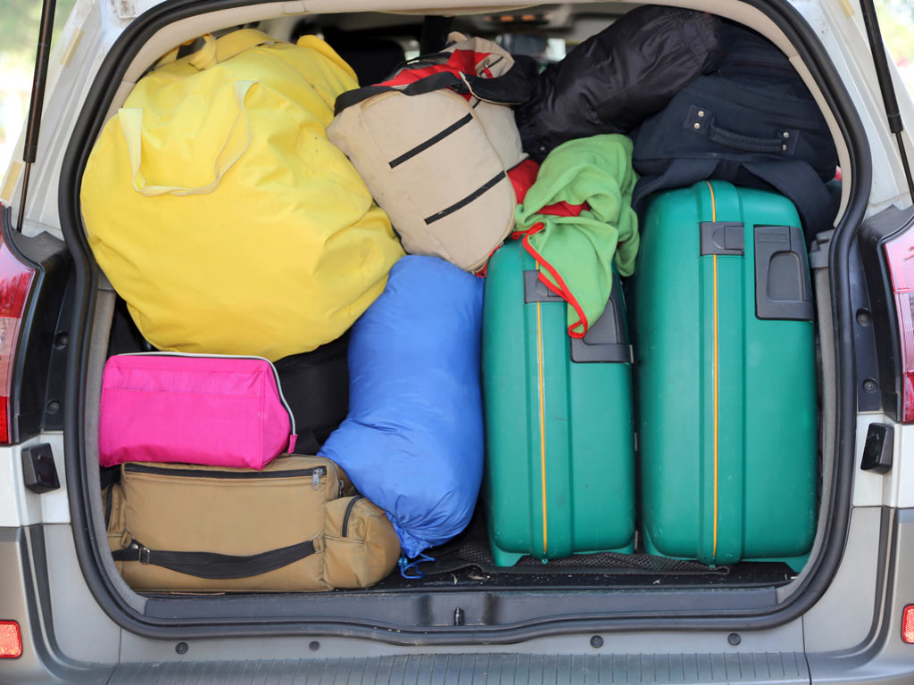 Car trunk packed with colorful luggage for moving abroad cheaply.