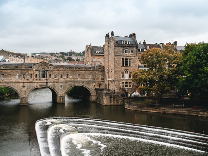 Arched stone bridge over river with small waterfalls in Bath, UK