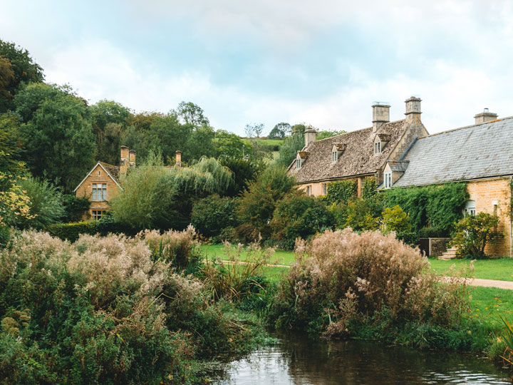 Three stone cottages in front of grassy pond in Cotswolds, visited after learning how to move to the UK