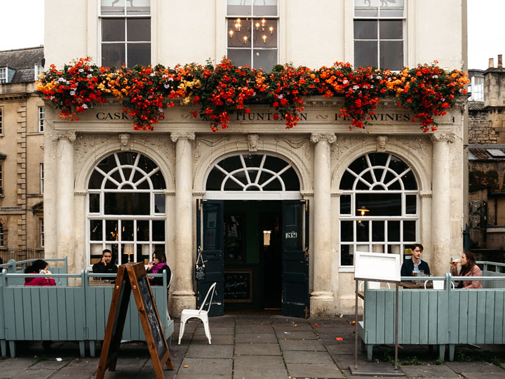 Facade of The Huntsman pub with red and yellow flowers hanging over door and blue fence in front