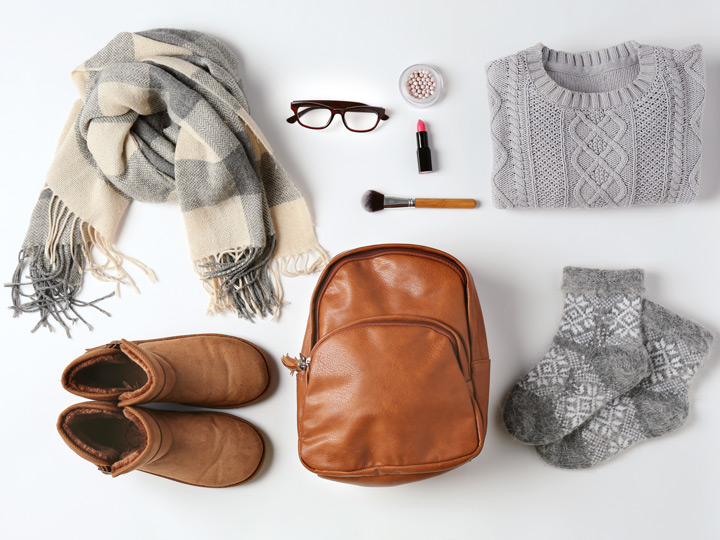 Flat lay of sweater, backpack, socks, boots, scarf, and other things to wear on a long flight in economy.