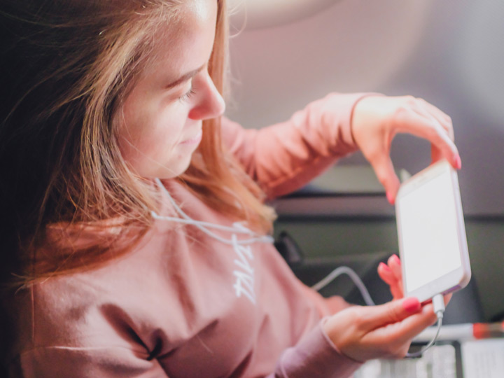Girl in pink sweater reading on smartphone to survive long haul flight in economy.