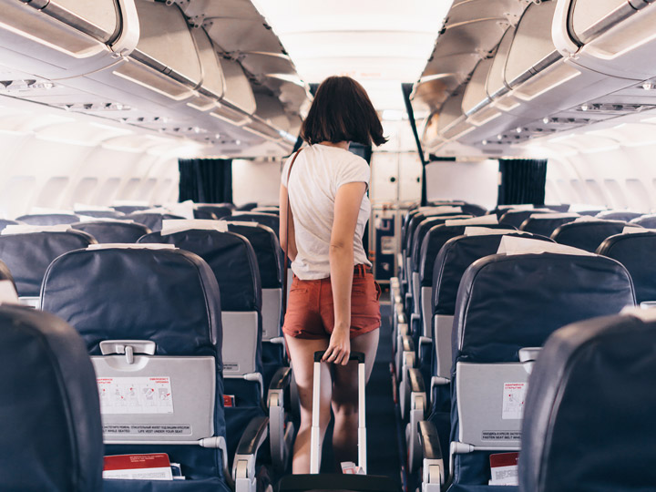 How to survive long flights in economy - girl walking down airplane aisle pulling suitcase.