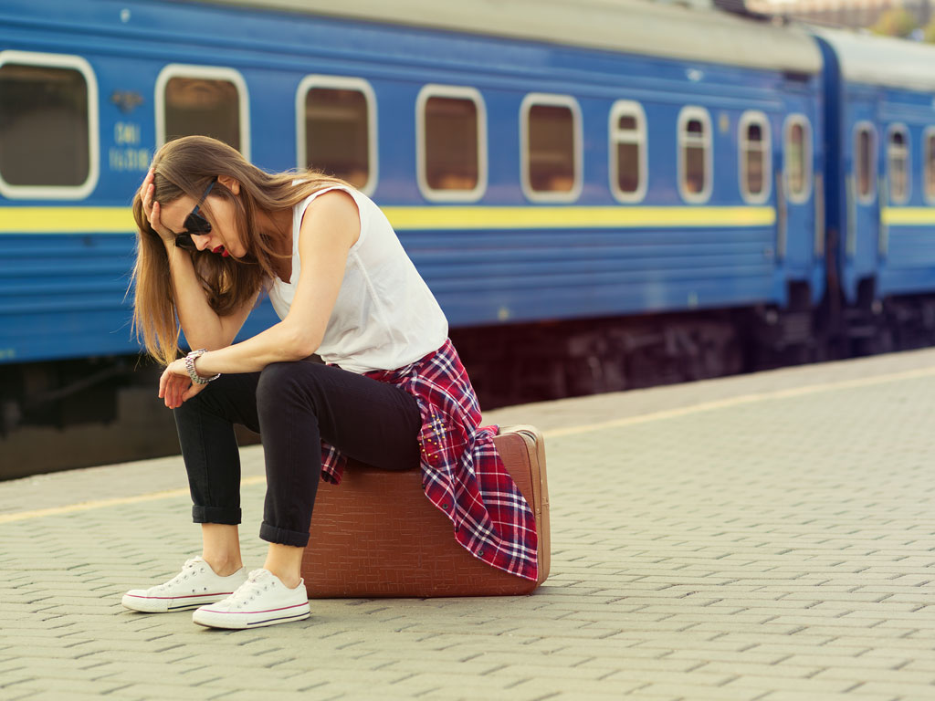 Woman sitting on suitcase looking at watch, making international travel mistake of missing train.