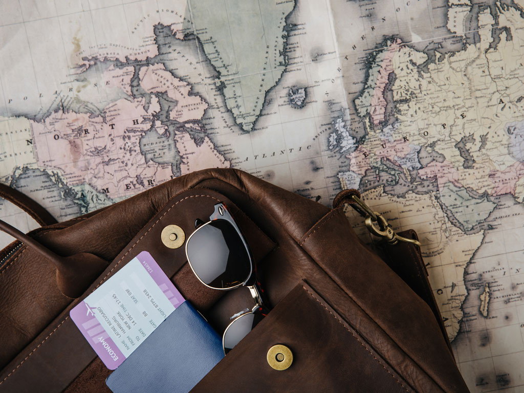 Leather bag with passport and glasses sitting on top of old map.