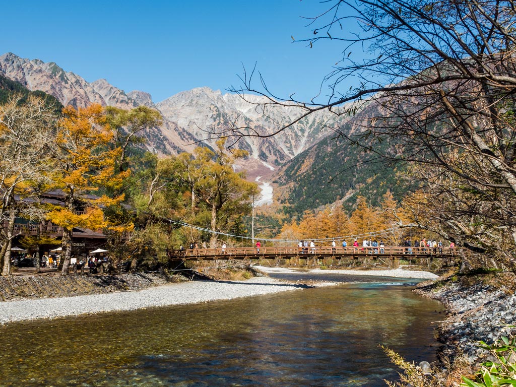 Wooden bridge crossing river with mountain backdrop in Kamikochi park.