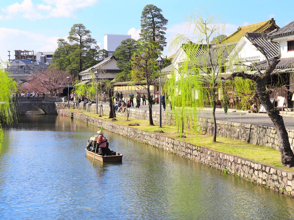 Traditional boat traveling down canal lined with trees in Kurashiki Japan off the beaten path.