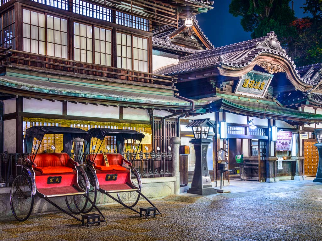 Nighttime exterior of Dogo Onsen in Matsuyama with two red rickshaws out front.