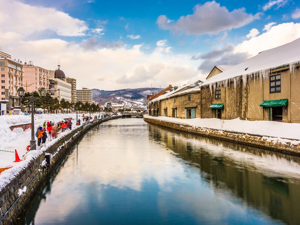 Wintery scene of Otaru canal and warehouses with partly cloudy sky.