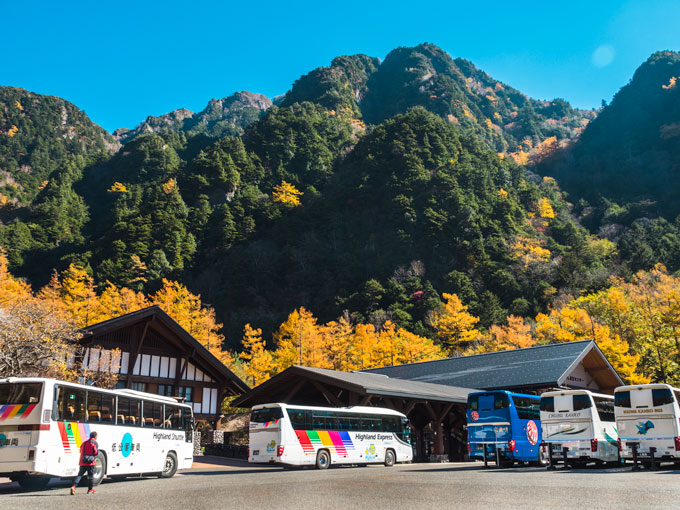 Kamikochi Bus Terminal beneath tree-lined mountain.