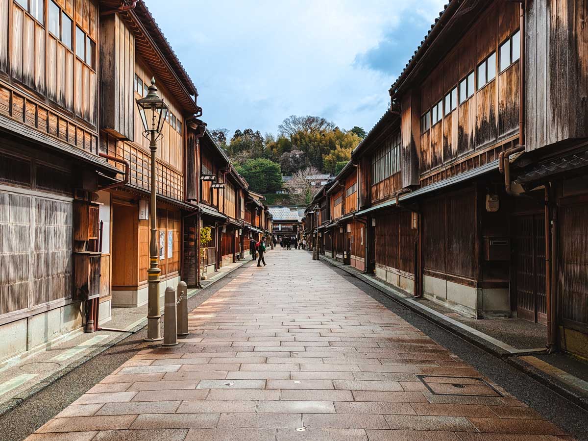 Historic Japanese street with wet wooden buildings and travelers following Kanazawa day trip itinerary.