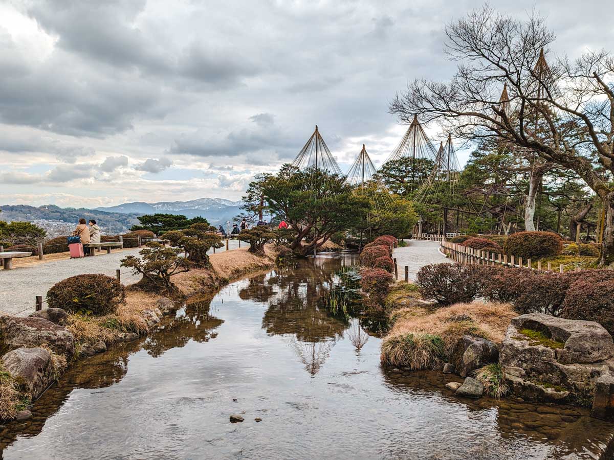 Pond, walking trails, shrubs, and view of mountains in distance inside Kenrokuen Garden Kanazawa.