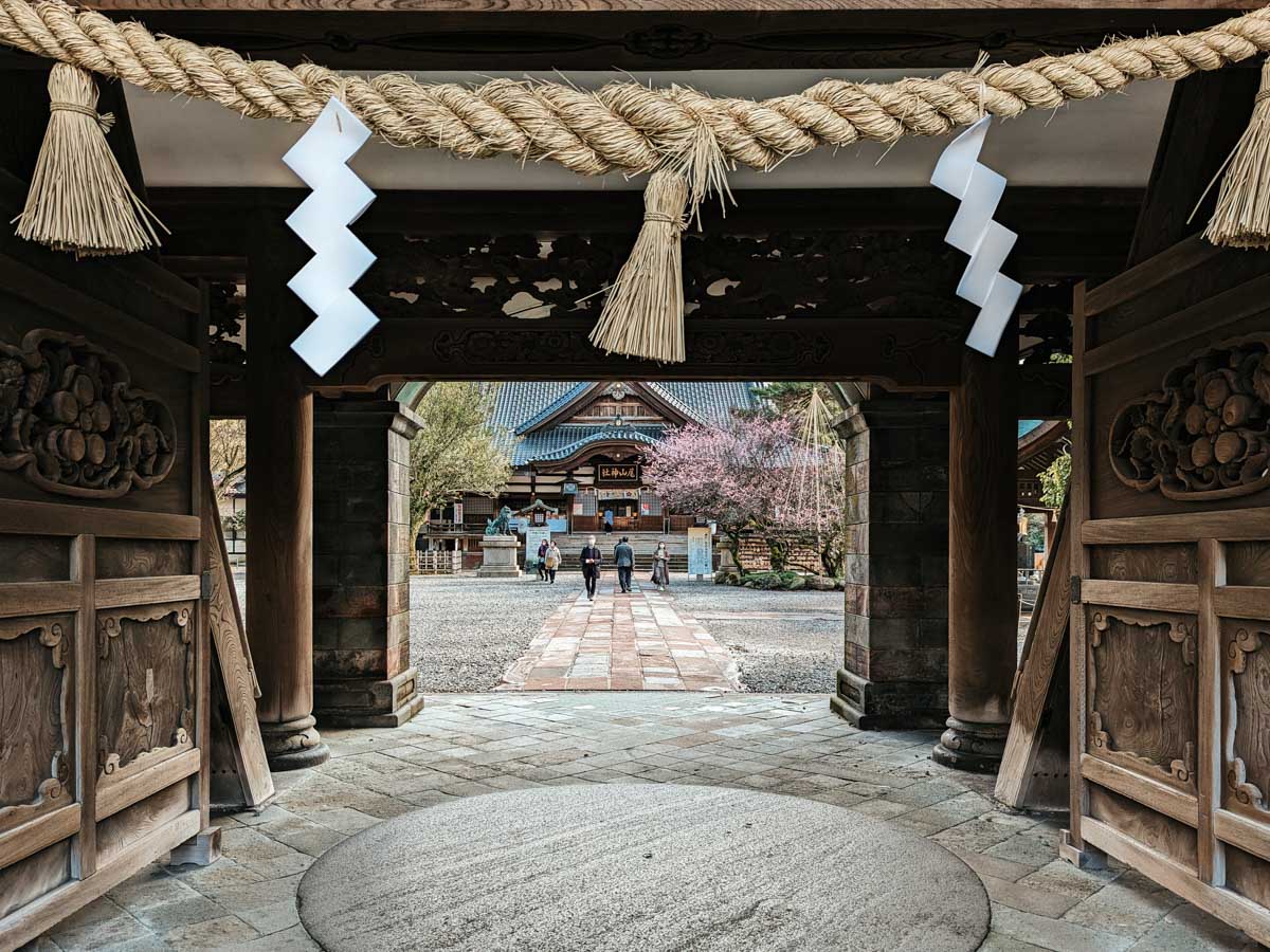 View of Kanazawa Oyama Shrine through carved wooden gate and shimenawa.