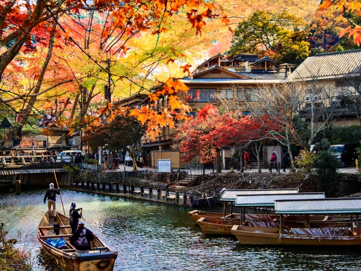 Arashiyama river with traditional boats and autumn leaves overhead.