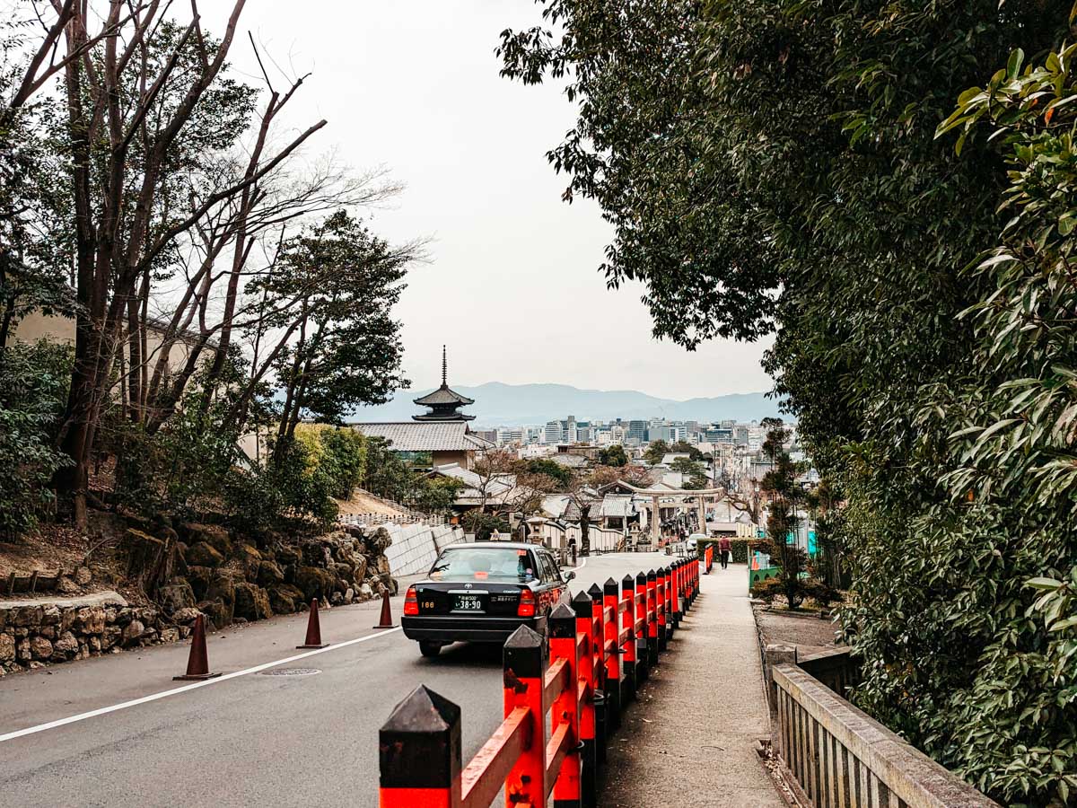 Black taxi driving down tree-lined street towards central Kyoto.