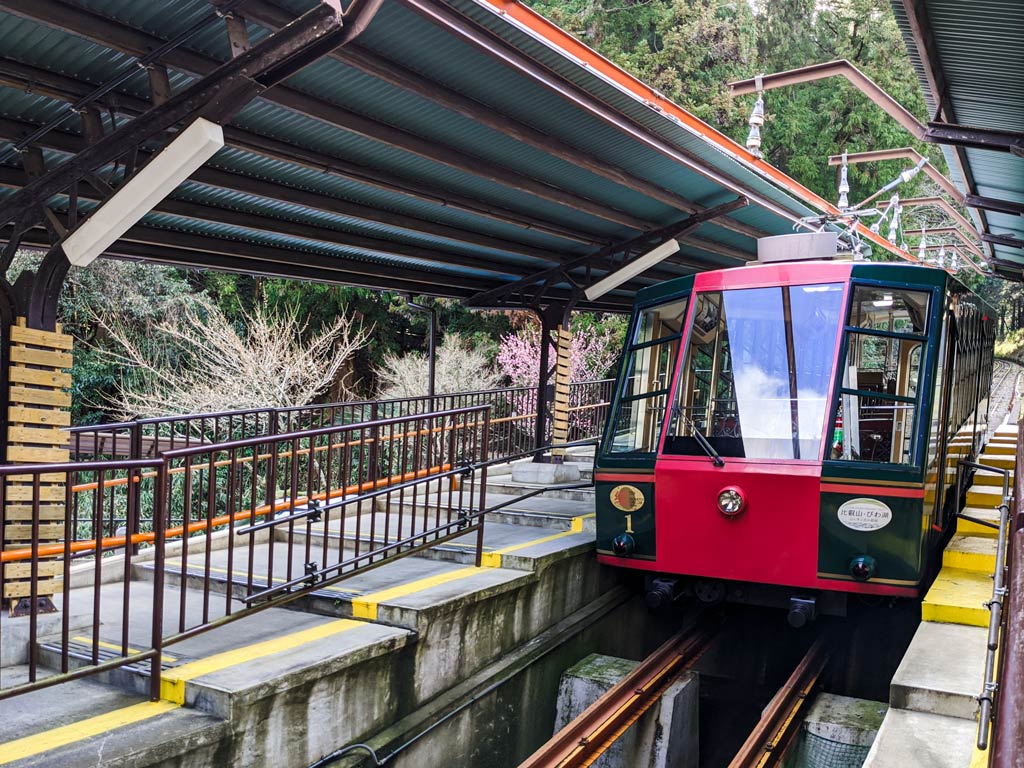 Red and green cable car pulling into open air station at Cable Sakamoto.