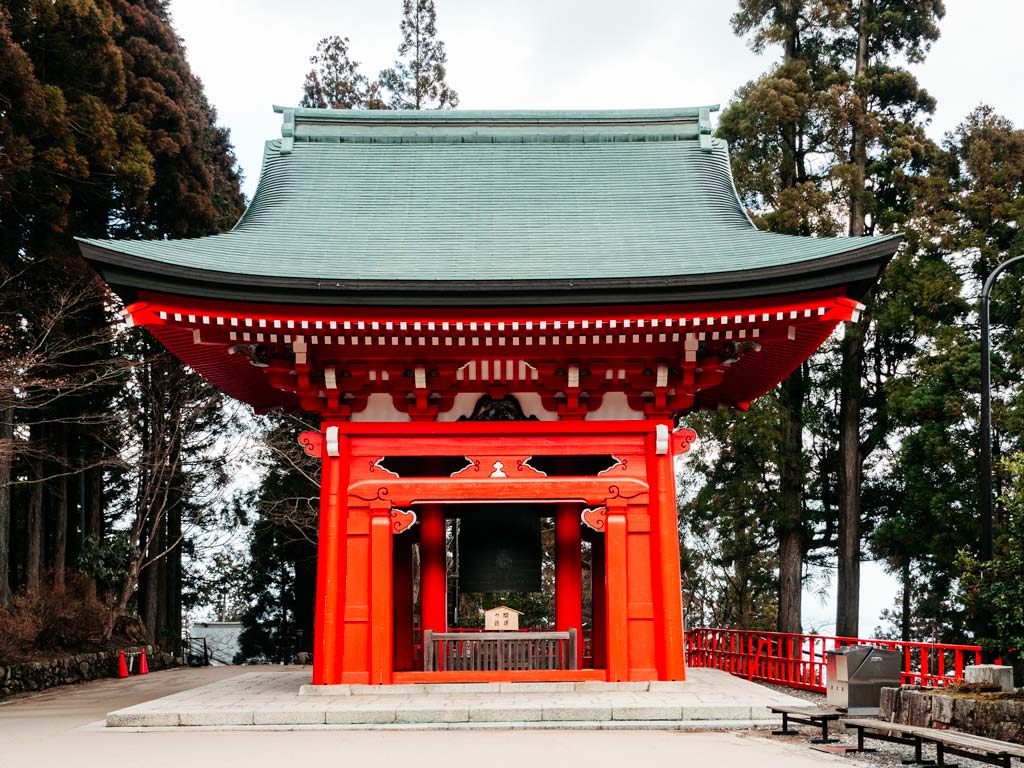Traditional Japanese shrine bell building with red facade and green roof.